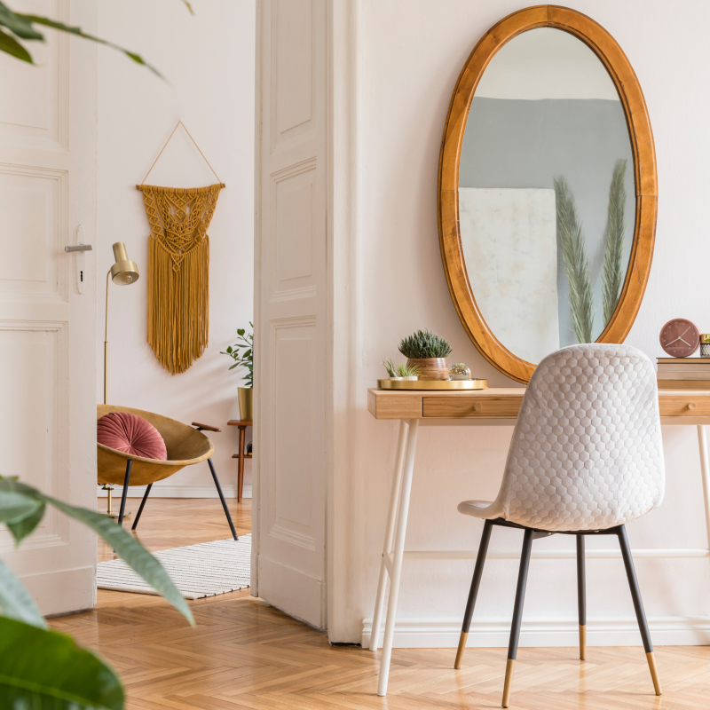 Stylish and minimalist interior of living room with design gold armchair, lamp, poster frames. dressing table with mirror, plants, yellow macrame and accessories in cozy home decor.